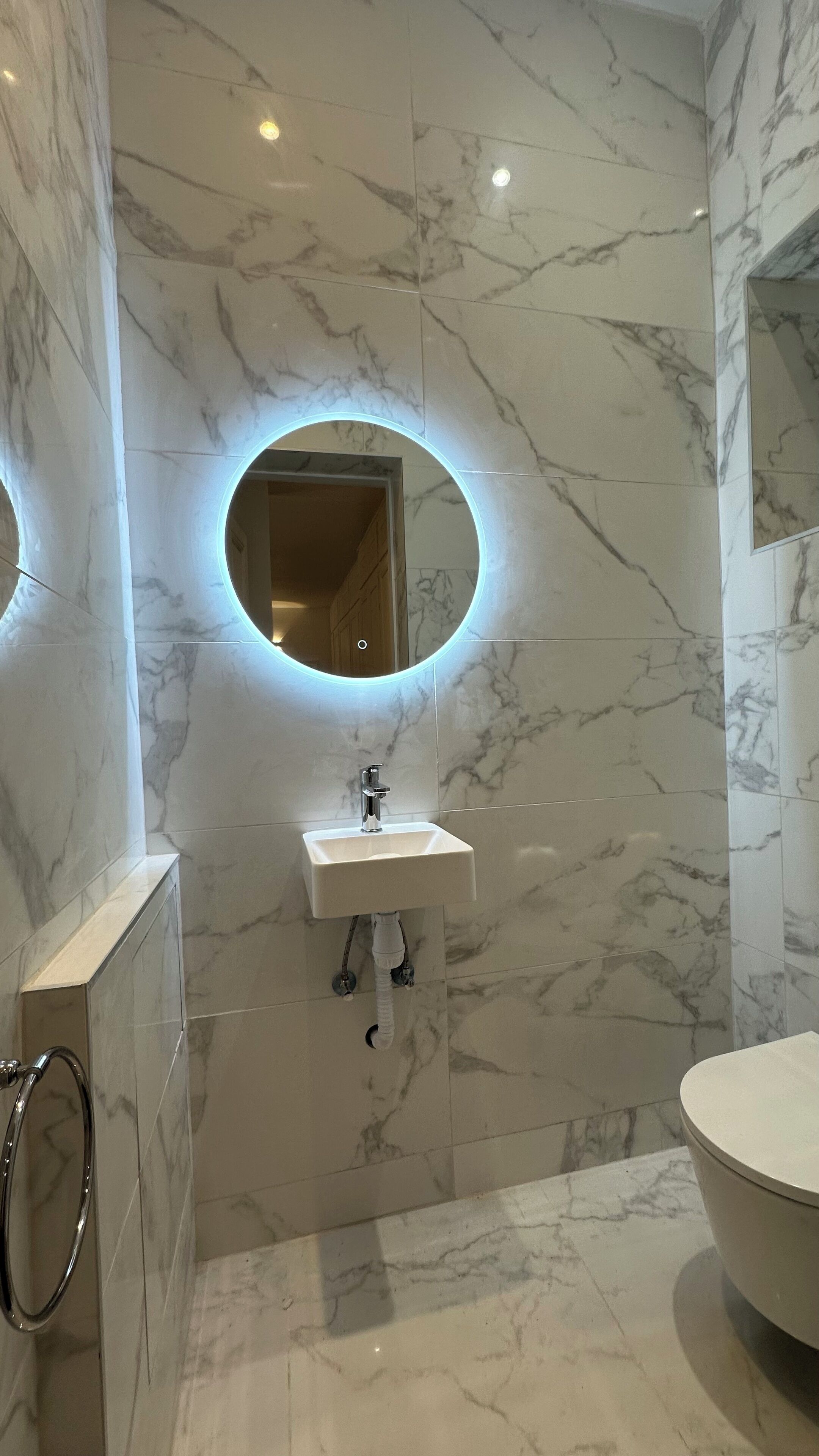 Un baño con piso de mármol, un lavamanos con espejo y un inodoro.