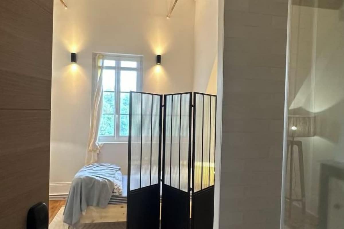 Una habitación con cama, ventana con cortinas y un separador negro.