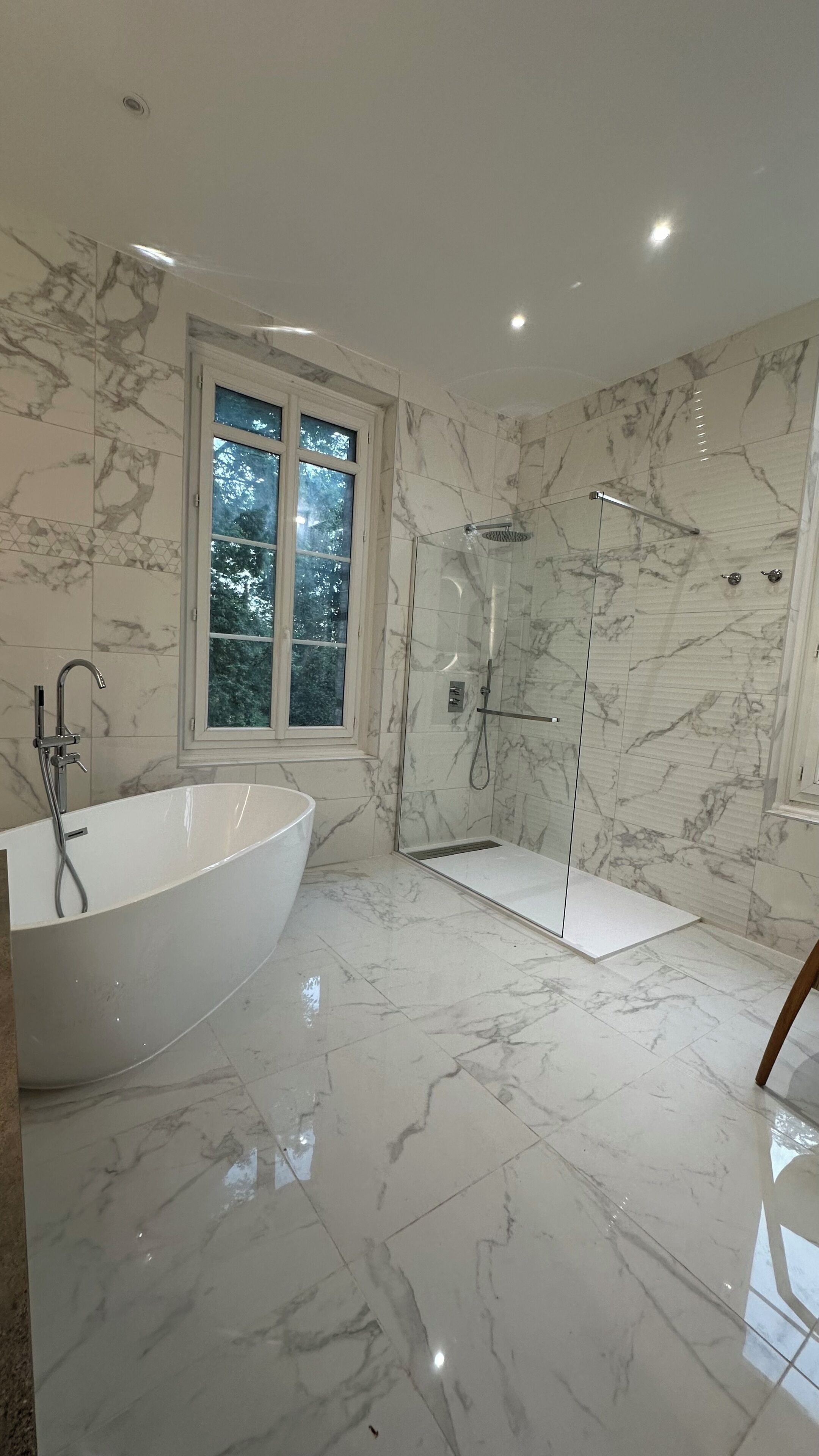 Un baño moderno con una bañera independiente, ducha envuelta en vidrio y ventana que proporciona luz natural.