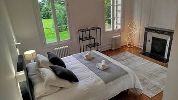 Een slaapkamer met een bed, nachtlampjes, een radiator, een open haard en uitzicht op de tuin door het raam.