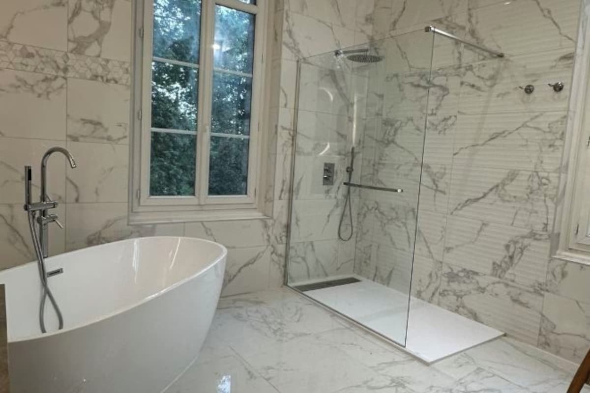 A bathroom with a freestanding bathtub, a glass-enclosed shower, and marble flooring.