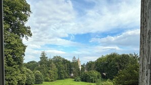 A view of a well-maintained lawn with a stone structure in the distance, surrounded by dense trees. - Chateau Loyd&Spa Normandie Pays de Caux (Les Hauts-de-Caux)