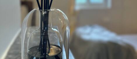 A clear glass vase with a water-filled base and black reed sticks on a marble countertop.