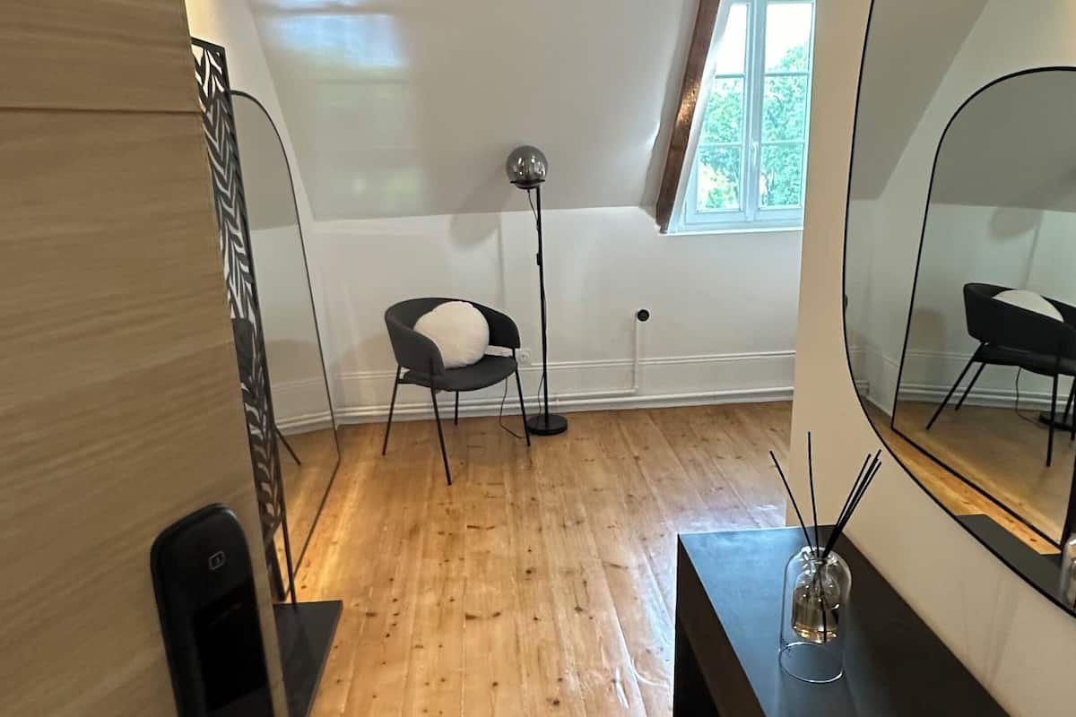 A modern attic bedroom with wooden floors, a large mirror, a desk, and a chair.