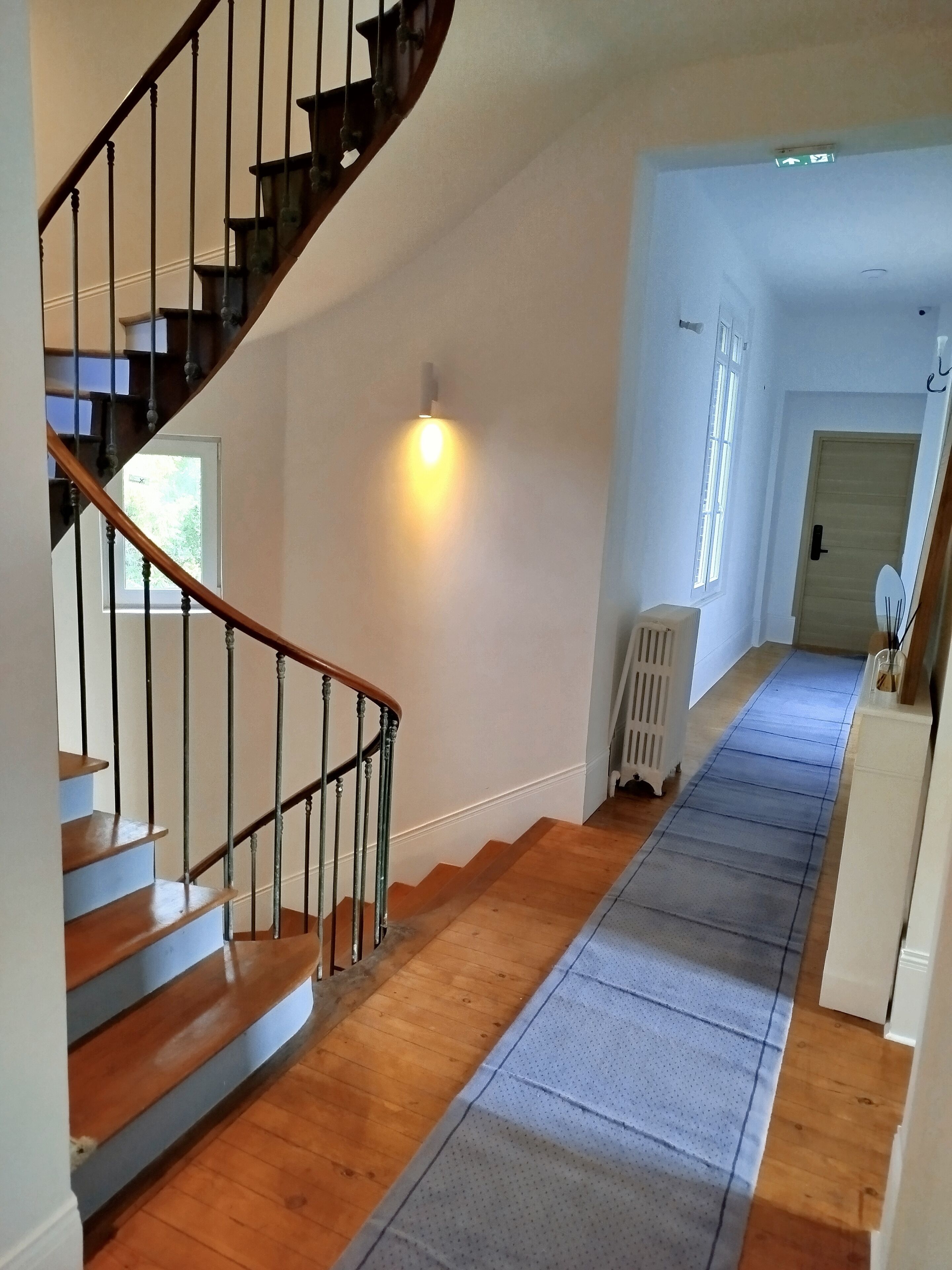 Una escalera con escalones de madera y barandillas metálicas que lleva a un rellano con una lámpara.