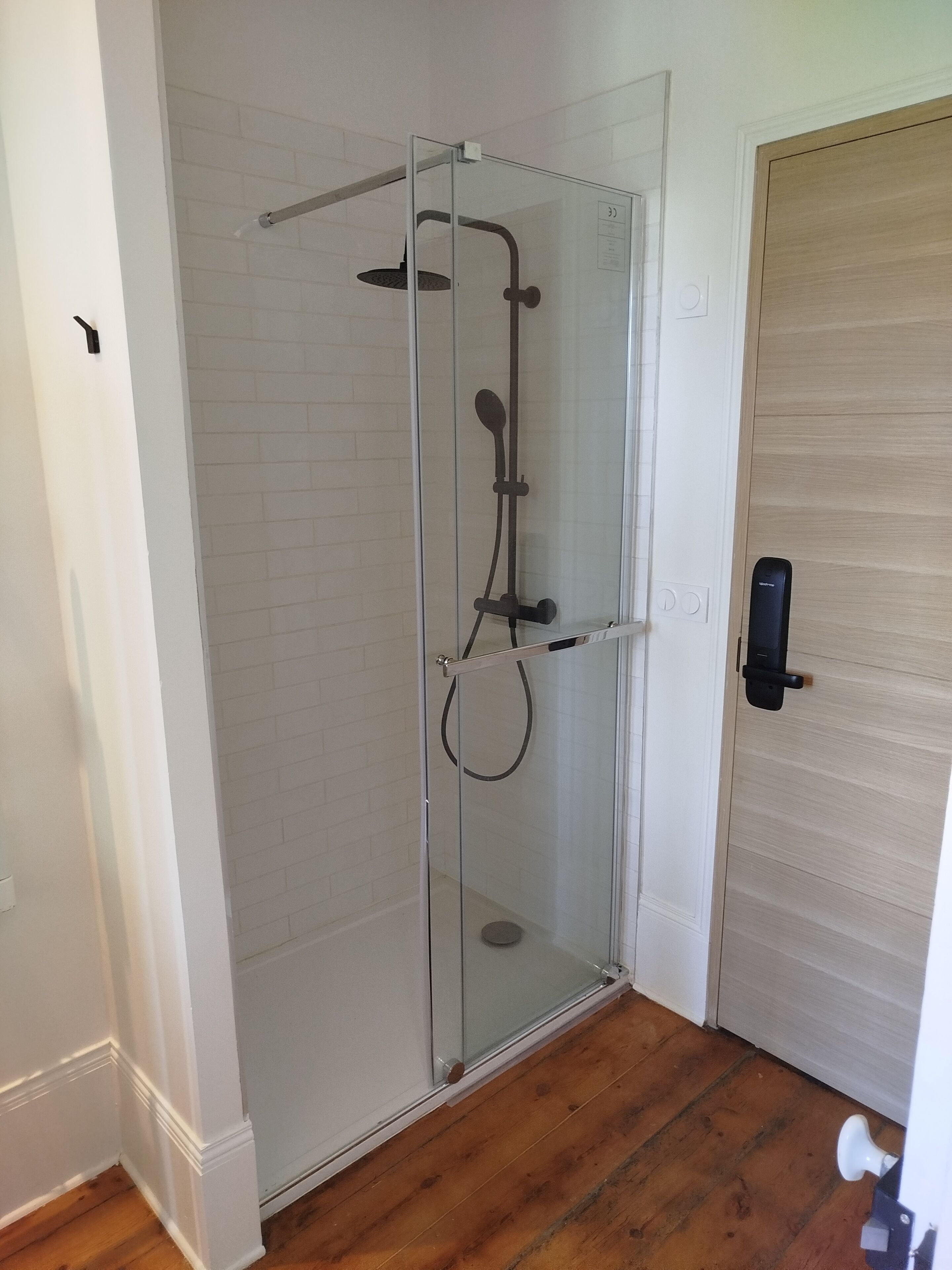 Une douche fermée par des parois en verre, dotée d’un pommeau de douche à main et d’un flexible de douche à main.