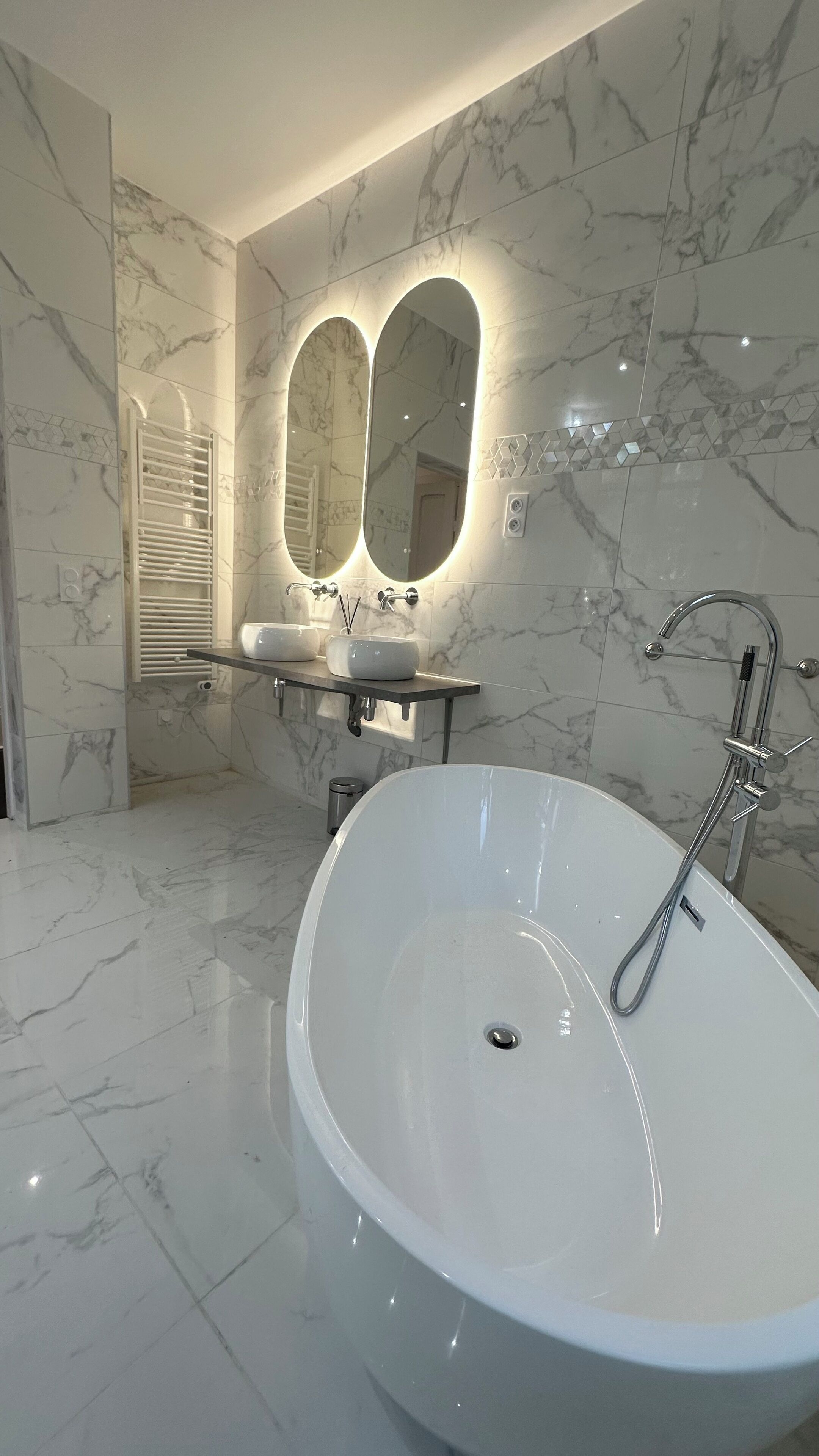 Un baño moderno con una bañera independiente, dos espejos montados en la pared y un mueble de tocador con lavabo.