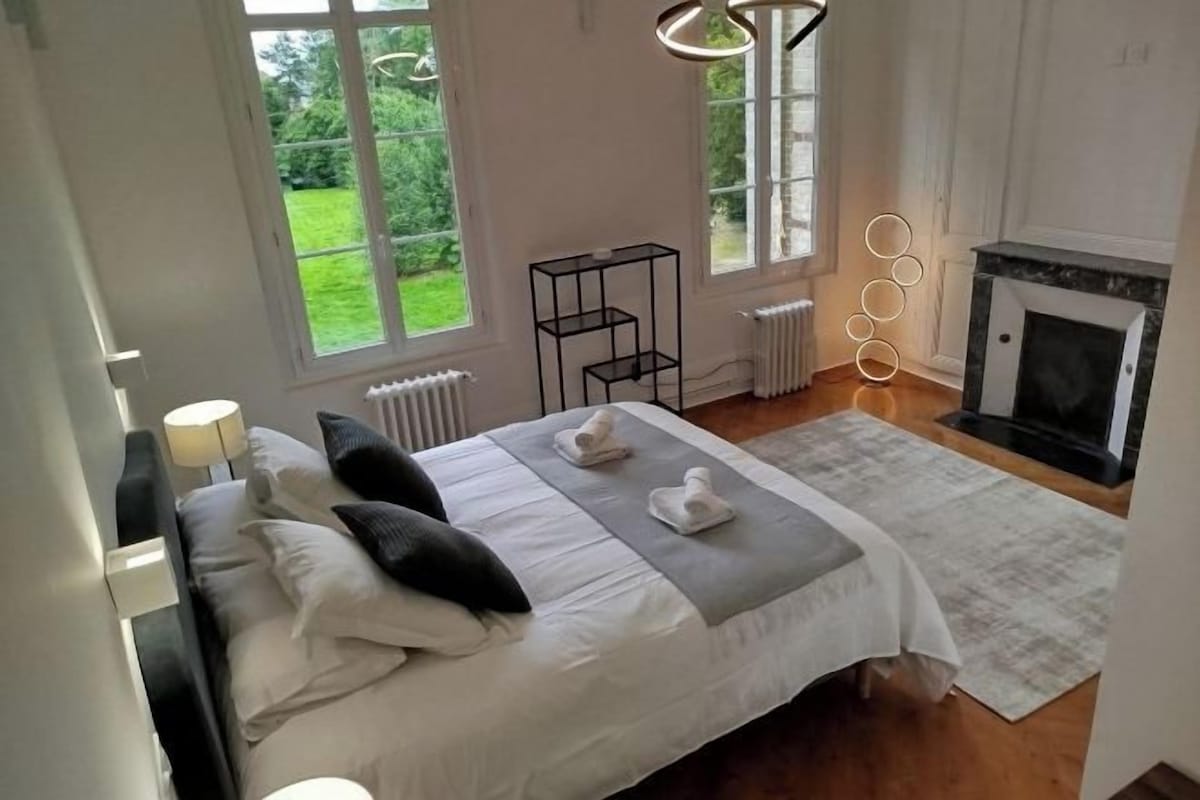 A bedroom with a bed, a fireplace, and a view of greenery outside.