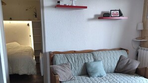 A cozy living room with a wooden sofa, a small rug, and a wall-mounted shelf with decorative items.
