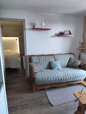 A cozy living room with a wooden sofa, a small rug, and a wall-mounted shelf with decorative items.