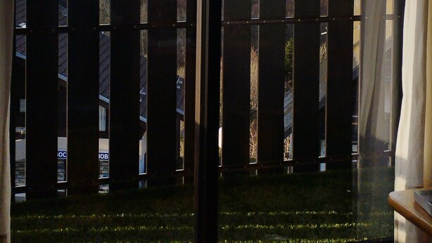 A view through a window with a wooden railing, overlooking a lake and distant hills.