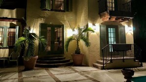 Un edificio de dos pisos con un patio empedrado, plantas en macetas y una piscina.