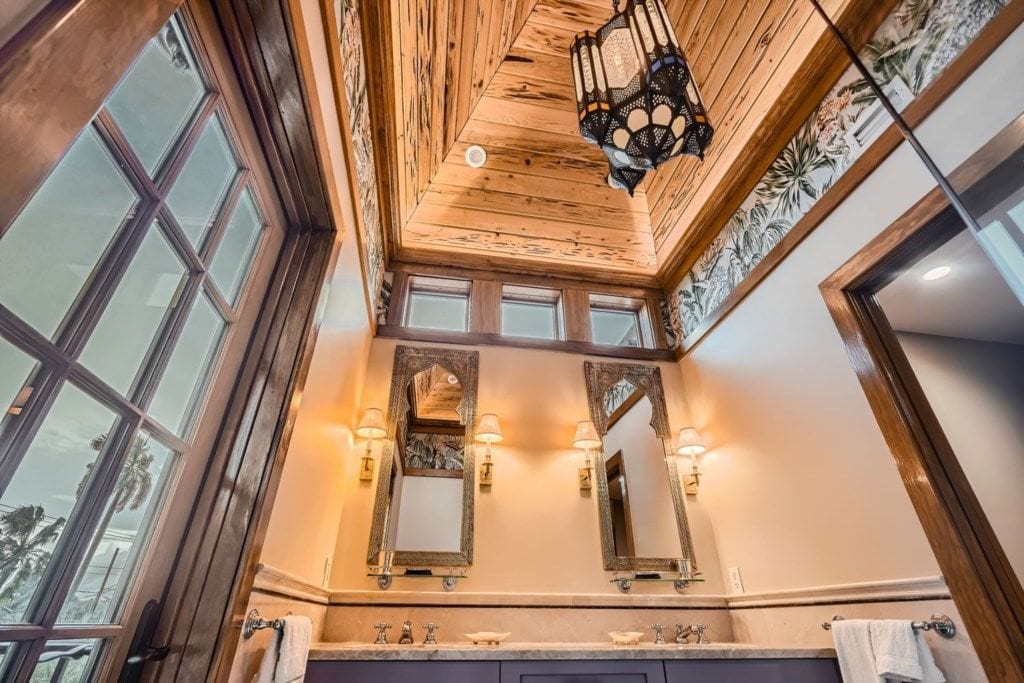 Une salle de bain avec un plafond en bois, de grandes fenêtres et deux miroirs fixés au mur, équipés de luminaires.