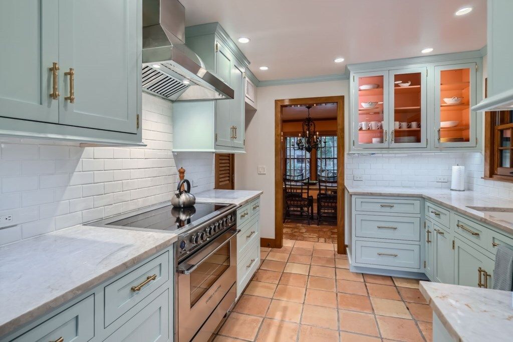 Una cocina con gabinetes azul claro, una estufa de acero inoxidable y piso de baldosas.
