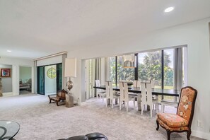 A spacious living room with a dining area, large windows, and a view of greenery.