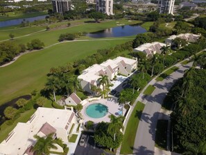 A residential area with a swimming pool surrounded by a lawn and palm trees.