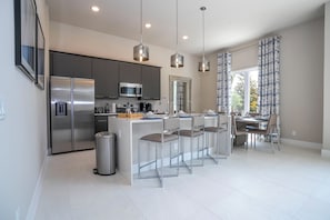 Una cocina moderna con electrodomésticos de acero inoxidable, una isla central con taburetes de bar e iluminación colgante.