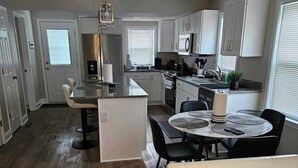 Una cocina moderna con armarios blancos, una isla central y un comedor con una mesa redonda y sillas.