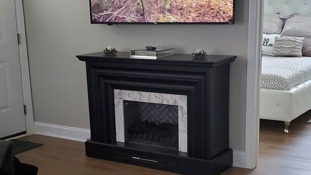Una sala de estar moderna con chimenea, un televisor montado encima y una cama con cabecera blanca.