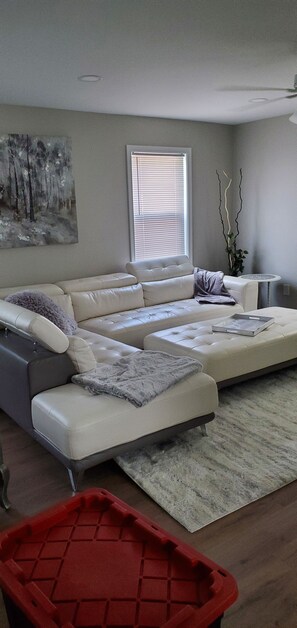 A modern living room with a sectional sofa, a small side table, a painting on the wall, and a window with blinds.