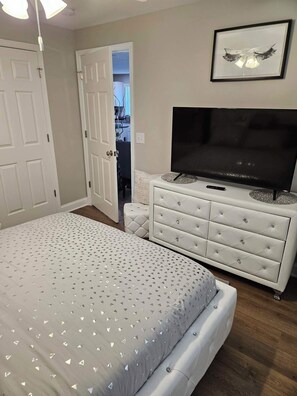 A bedroom with a bed, a TV, a dresser, and a door leading to another room.