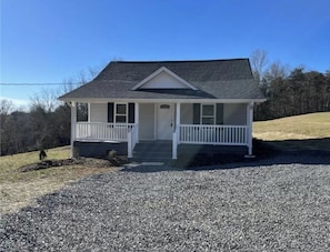 A single-story house with a front porch, a small front yard, and a gravel driveway.