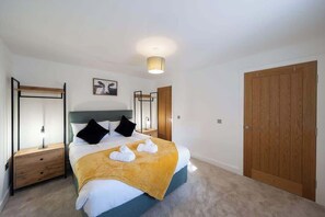 A hotel room with a bed, two bedside tables, a wooden wardrobe, a ceiling light, and a framed picture on the wall.
