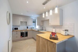 A modern kitchen with white cabinets, a wooden countertop, a microwave, a toaster, and hanging pendant lights.