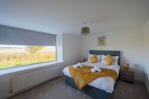 A bedroom with a bed, a window, a radiator, a nightstand, and a wall-mounted lamp.