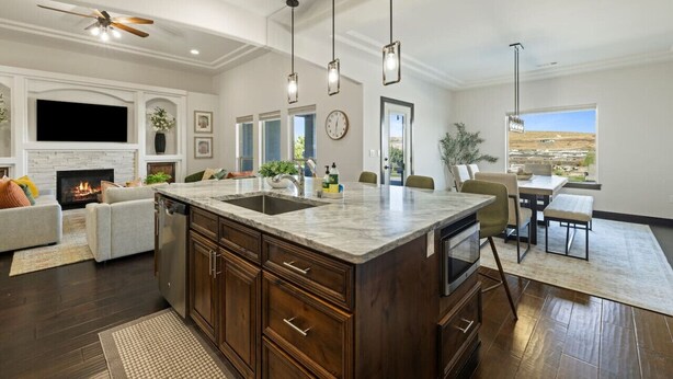 A modern kitchen with a large island, dark wood cabinets, and pendant lighting.