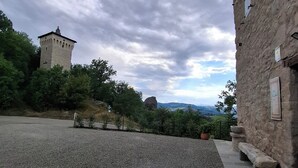 A courtyard with a stone building, a tower, and a view of distant mountains. - Il Castellaro ai Sassi (Guiglia)