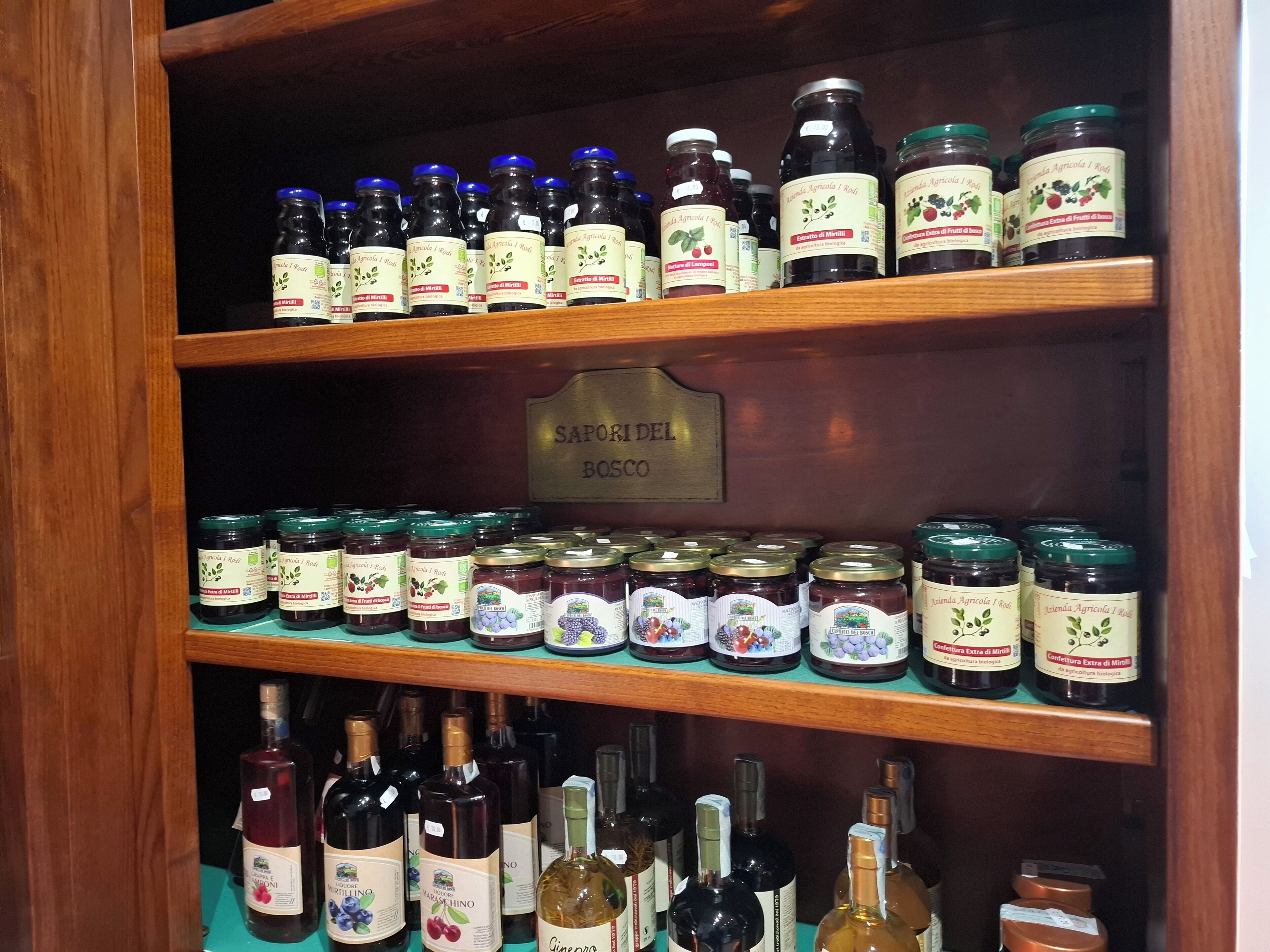 A wooden shelf with various jars and bottles of food products, including preserved fruits and wines.