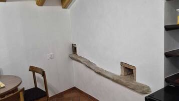 Ein Zimmer mit Holzbalkendecke, einem kleinen Tisch mit Stuhl, einem Einbauschrank und einem schwarzen Schrank.
