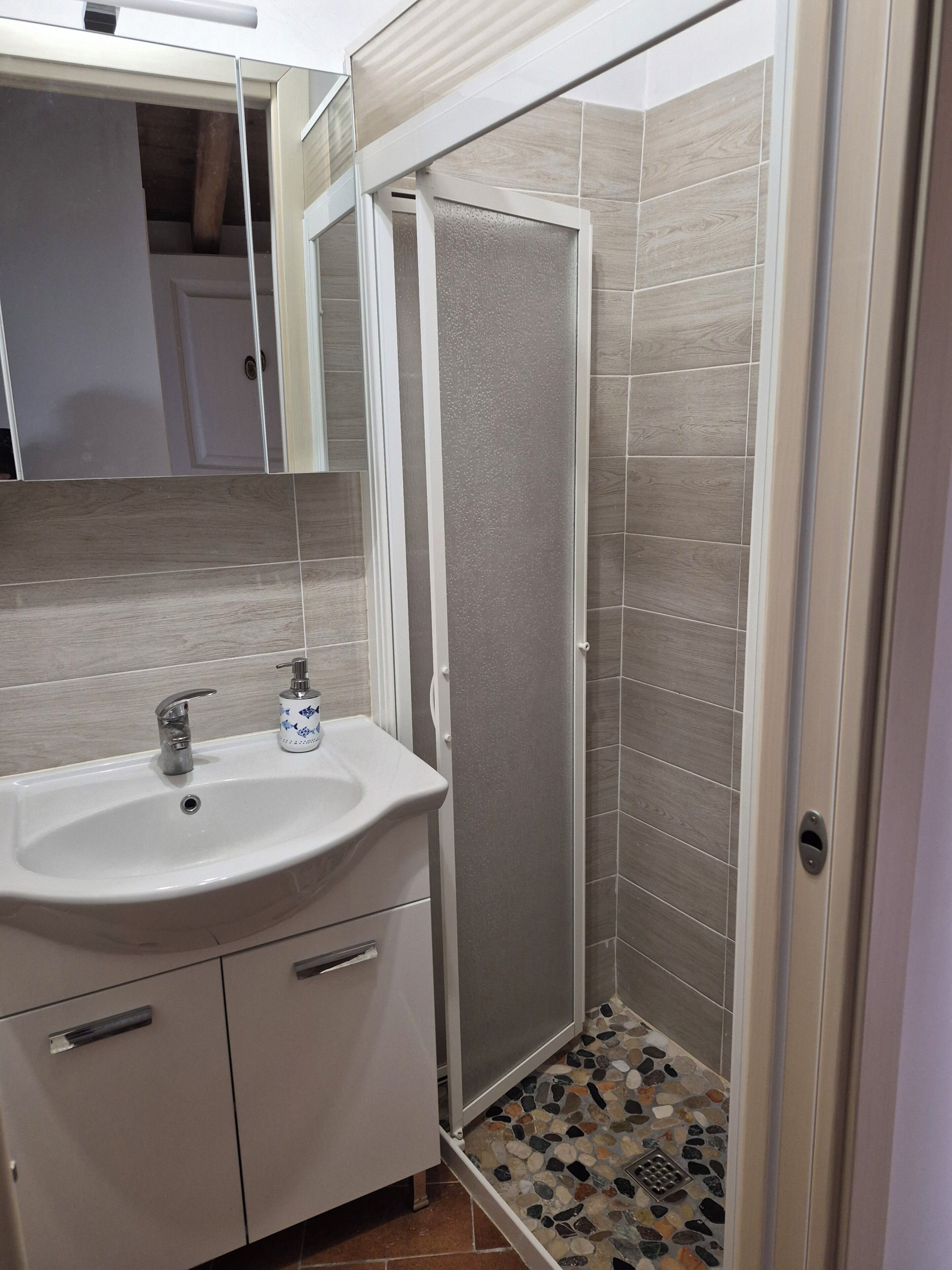 A bathroom with a white sink, a mirror, a shower enclosure, and tiled walls.