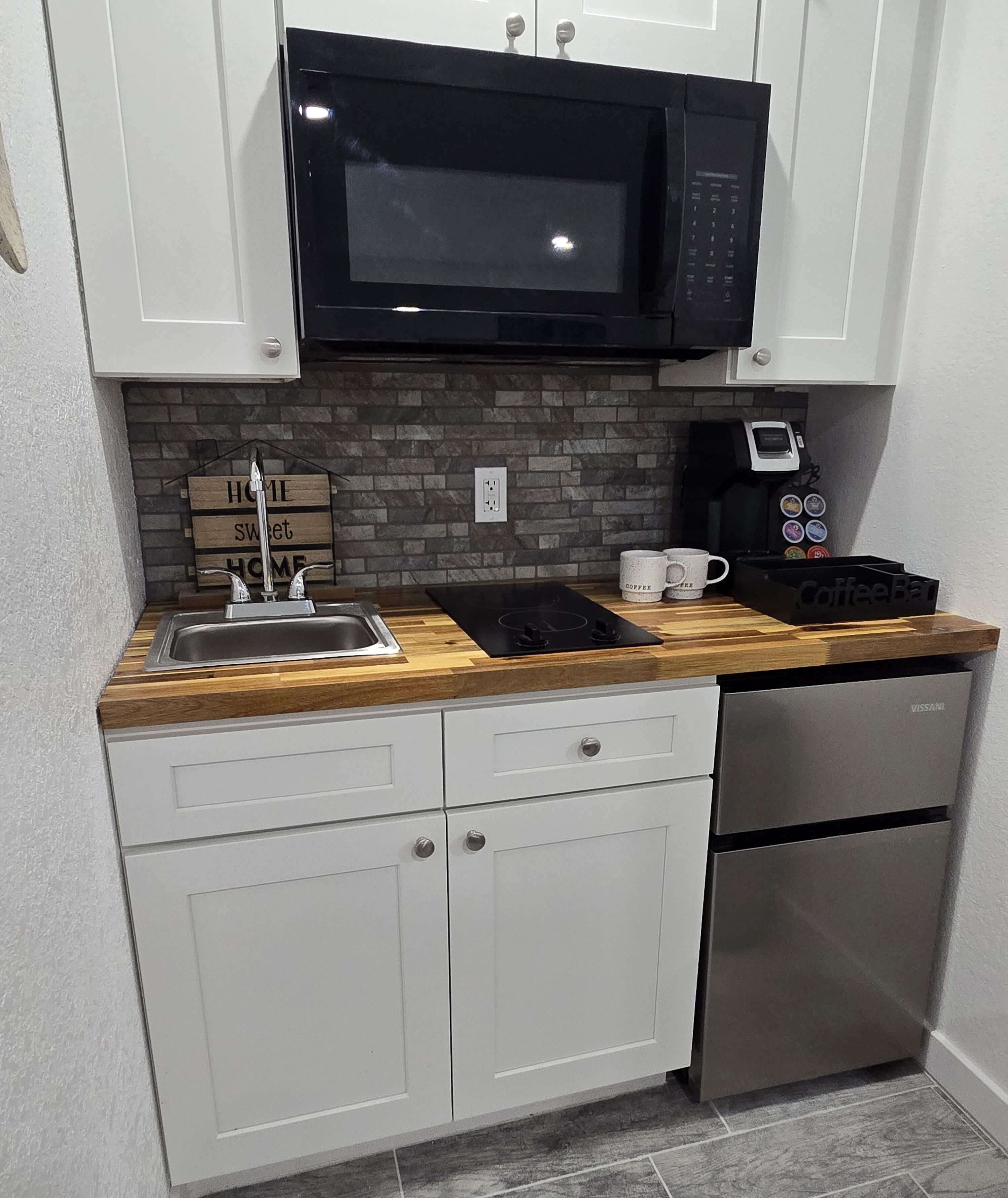 A compact kitchen with a stainless steel dishwasher, a black microwave, and a coffee machine.