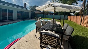 A backyard with a swimming pool, a patio table with chairs, and an umbrella.