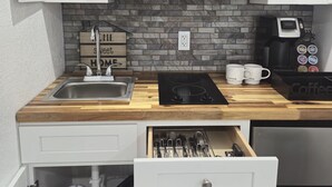A compact kitchen with white cabinets, a black microwave, a coffee maker, and a wooden countertop.