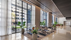 Eine geräumige Lobby mit großen Fenstern, einer Sitzecke mit Sofas und Sesseln sowie mehreren Blumentöpfen.