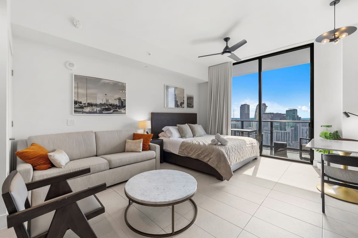 Ein modernes Hotelzimmer mit Bett, Sofa, rundem Tisch und einem Balkon mit Blick auf die Stadt.