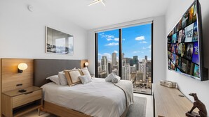 Ein modernes Schlafzimmer mit Blick auf die Stadt, ein großes Bett, Nachttische und ein wandmontierter Fernseher.