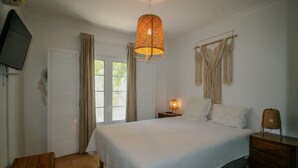 Une chambre à coucher avec un lit, une table de chevet, une lampe, un téléviseur et une fenêtre avec des rideaux.