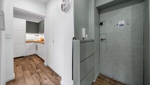 A modern kitchen with white cabinets, a wooden floor, and a grey door with a small window.