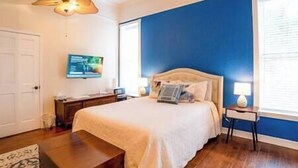 Quarto com cama, mesas de cabeceira, televisão e janela.
