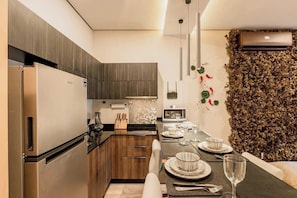 A modern kitchen with a built-in refrigerator, microwave, and stove. There is a dining area with a table set for two, and a decorative wall with foliage.