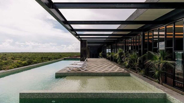 A modern infinity pool with a clear view of the landscape, a covered walkway, and a building with large windows. - Amira Itzamna Luxe Studio Close to beach! (Tulum)