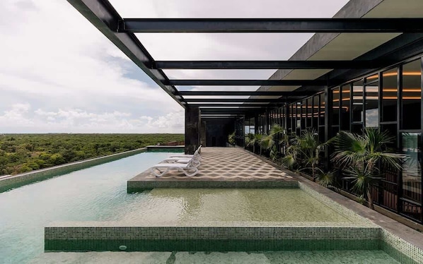 A modern infinity pool with a clear view of the landscape, a covered walkway, and a building with large windows.