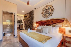 A modern bedroom with a large bed, a wooden headboard, a wall-mounted artwork, and a bathroom visible through a glass door.