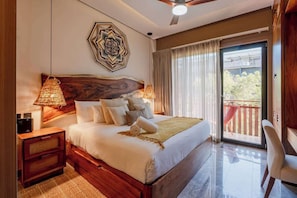 A bedroom with a large bed, a nightstand, a lamp, a ceiling fan, and a view of the outside.