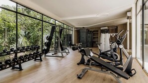 A gym with weightlifting equipment, cardio machines, and large windows offering a view of greenery. - Amira Itzamna Luxe Studio Close to beach! (Tulum)