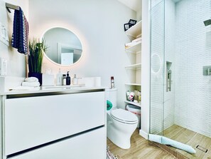 Ein modernes Badezimmer mit einem weißen Waschtisch, einem runden Spiegel, einer Toilette und einer Duschkabine.